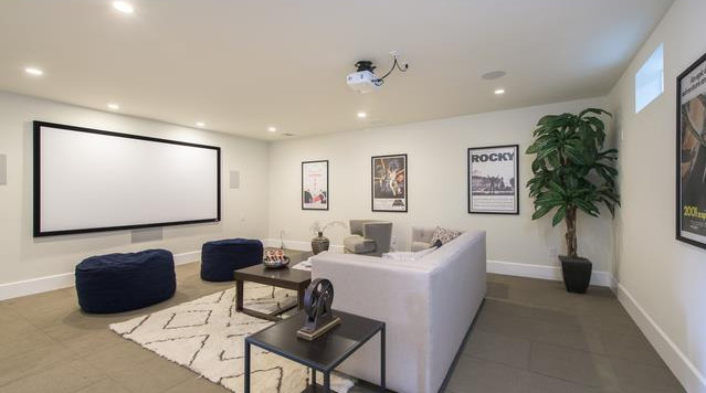 Design ideas for a large transitional enclosed home theatre in Los Angeles with beige walls, concrete floors, a projector screen and grey floor.