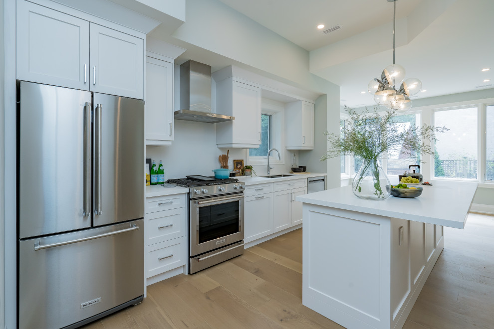 Inspiration for a mid-sized transitional galley light wood floor and beige floor eat-in kitchen remodel in Toronto with a double-bowl sink, shaker cabinets, white cabinets, quartz countertops, white backsplash, quartz backsplash, stainless steel appliances, an island and white countertops