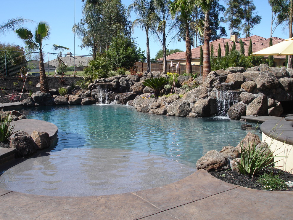 This is an example of a mid-sized contemporary backyard custom-shaped natural pool in Sacramento with a water feature and stamped concrete.