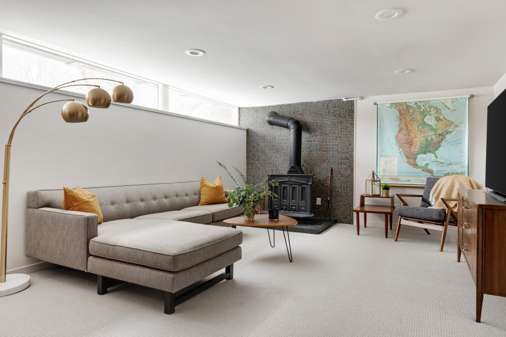 Cette image montre une salle de séjour vintage de taille moyenne avec un mur blanc, moquette, un poêle à bois, un manteau de cheminée en carrelage, un téléviseur fixé au mur et un sol gris.
