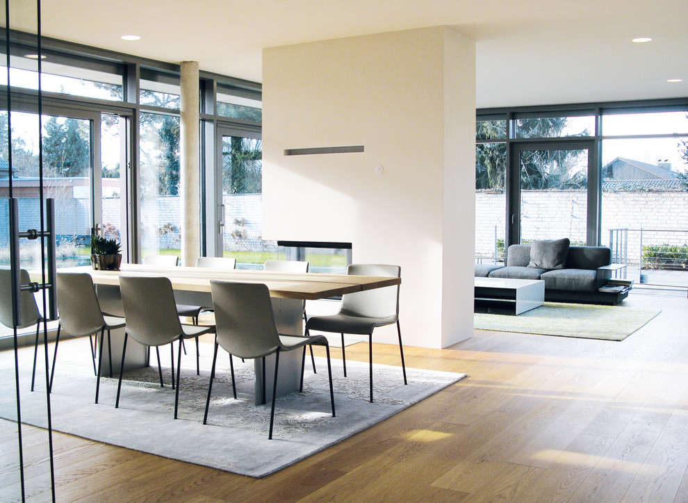 Inspiration for a large contemporary open plan dining in Stuttgart with white walls, light hardwood floors, a wood stove, a concrete fireplace surround and beige floor.
