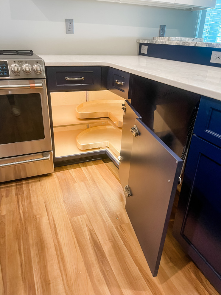 Foto de cocina minimalista de tamaño medio con armarios estilo shaker, puertas de armario azules, encimera de cuarcita, electrodomésticos de acero inoxidable, suelo de madera clara, península, suelo marrón y encimeras blancas