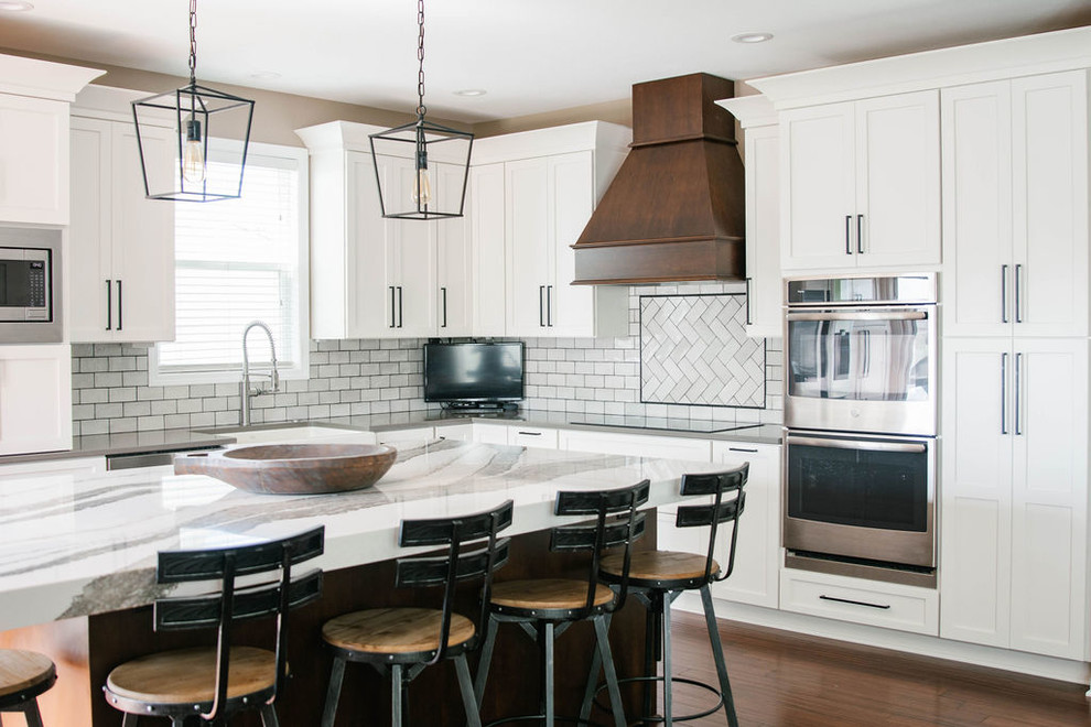 Inspiration for a mid-sized transitional l-shaped medium tone wood floor and brown floor eat-in kitchen remodel in Omaha with a farmhouse sink, shaker cabinets, white cabinets, quartzite countertops, white backsplash, subway tile backsplash, stainless steel appliances, an island and white countertops