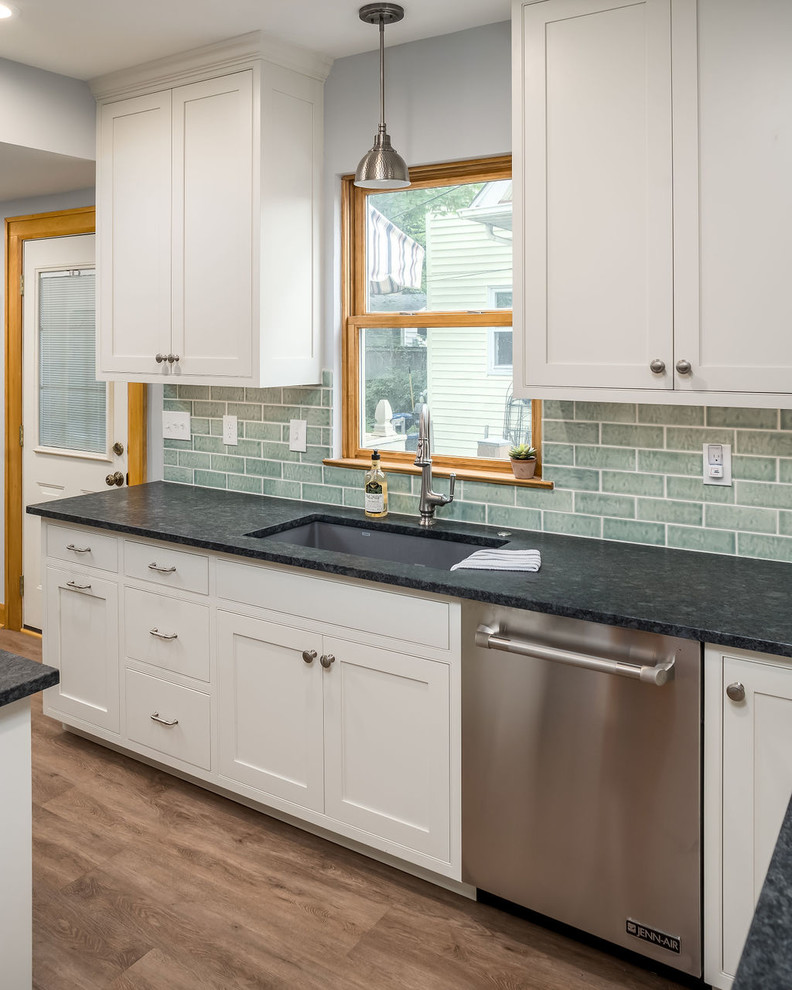 Photo of a mid-sized transitional galley eat-in kitchen in Columbus with an undermount sink, shaker cabinets, white cabinets, granite benchtops, green splashback, ceramic splashback, stainless steel appliances, vinyl floors, a peninsula, brown floor and black benchtop.