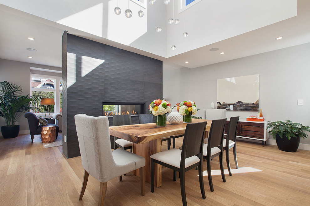 Large contemporary open plan dining in San Francisco with white walls, light hardwood floors, a two-sided fireplace and a concrete fireplace surround.