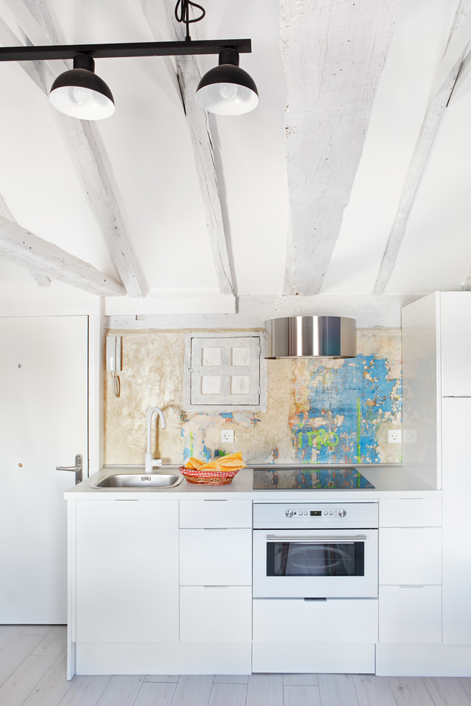 This is an example of a mid-sized country single-wall separate kitchen in Madrid with a drop-in sink, flat-panel cabinets, white cabinets, solid surface benchtops, multi-coloured splashback, stainless steel appliances, painted wood floors and no island.