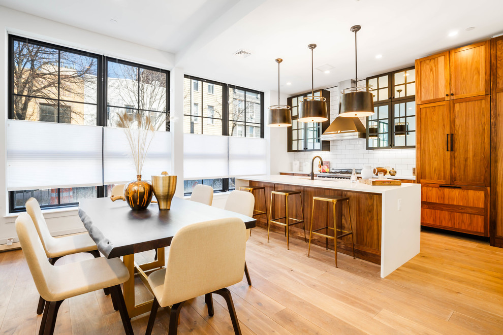 This is an example of a contemporary galley eat-in kitchen in New York with an undermount sink, shaker cabinets, medium wood cabinets, white splashback, subway tile splashback, panelled appliances, light hardwood floors, with island, beige floor and white benchtop.