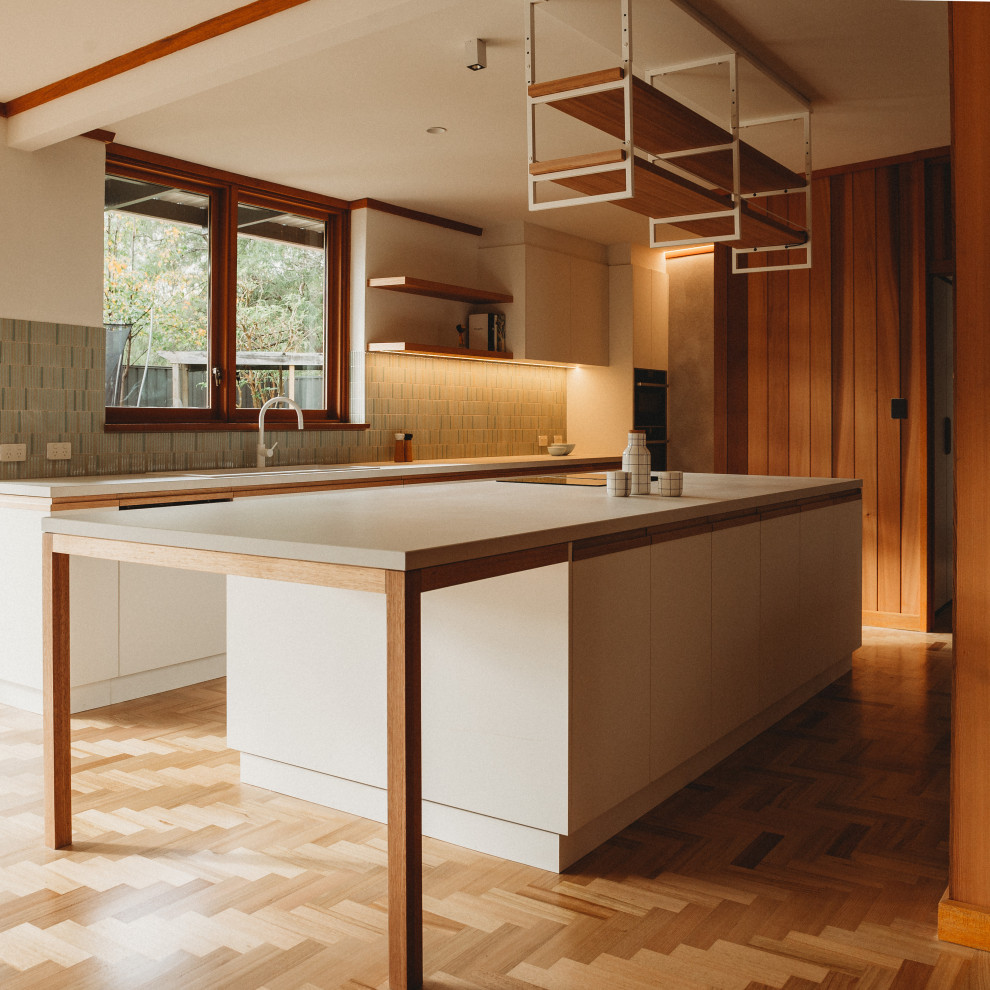 Large 1960s u-shaped medium tone wood floor, brown floor and exposed beam kitchen pantry photo in Adelaide with a double-bowl sink, flat-panel cabinets, white cabinets, quartz countertops, green backsplash, porcelain backsplash, white appliances, an island and white countertops