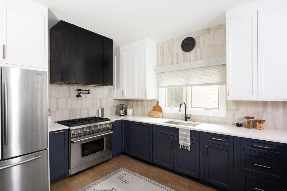 This is an example of a mid-sized transitional l-shaped eat-in kitchen in Chicago with a drop-in sink, shaker cabinets, white cabinets, quartz benchtops, grey splashback, ceramic splashback, stainless steel appliances, medium hardwood floors, a peninsula, brown floor and white benchtop.