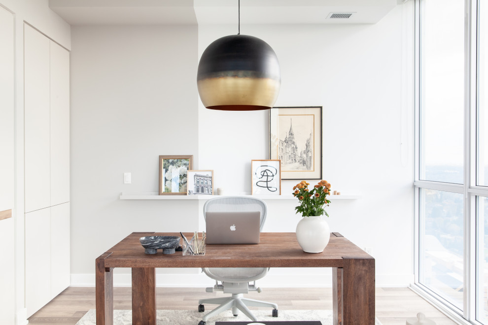 Modelo de despacho moderno pequeño con paredes beige, suelo laminado, escritorio independiente y suelo marrón