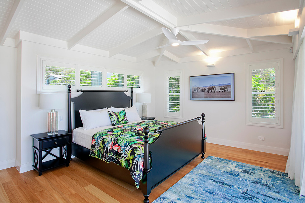 Mid-sized tropical master bedroom in Sunshine Coast with white walls and light hardwood floors.