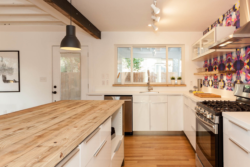 Inspiration for a mid-sized eclectic l-shaped eat-in kitchen in Austin with white cabinets, multi-coloured splashback, stainless steel appliances, light hardwood floors and with island.