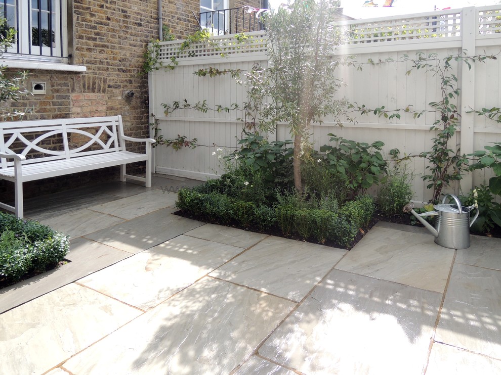 This is an example of a mid-sized contemporary backyard patio in London with natural stone pavers.