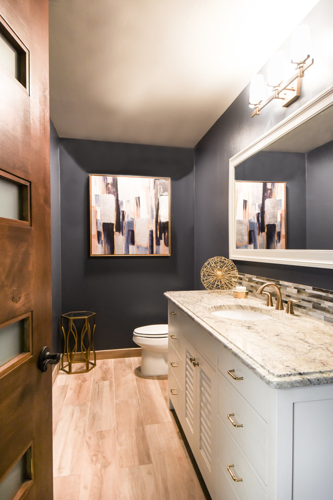 Photo of a large transitional powder room in Houston with louvered cabinets, white cabinets, blue walls, light hardwood floors, an undermount sink, granite benchtops, beige floor and grey benchtops.
