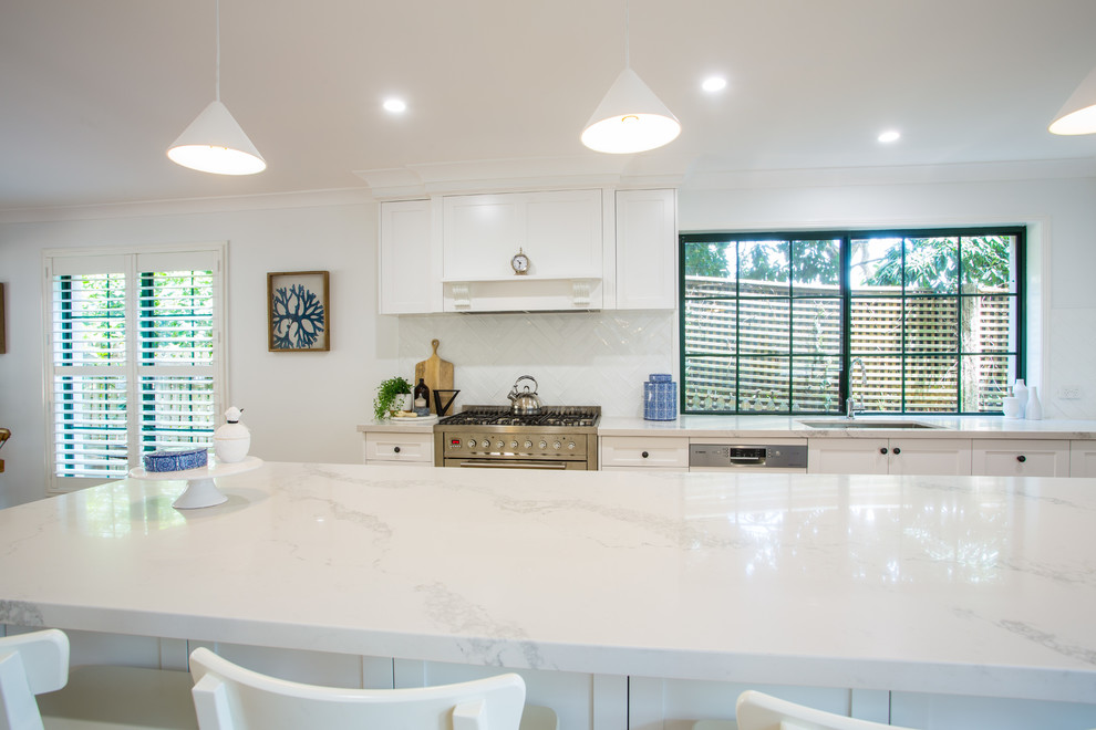 Design ideas for an expansive traditional galley eat-in kitchen in Brisbane with a single-bowl sink, shaker cabinets, white cabinets, solid surface benchtops, white splashback, subway tile splashback, stainless steel appliances, medium hardwood floors, with island, brown floor and white benchtop.