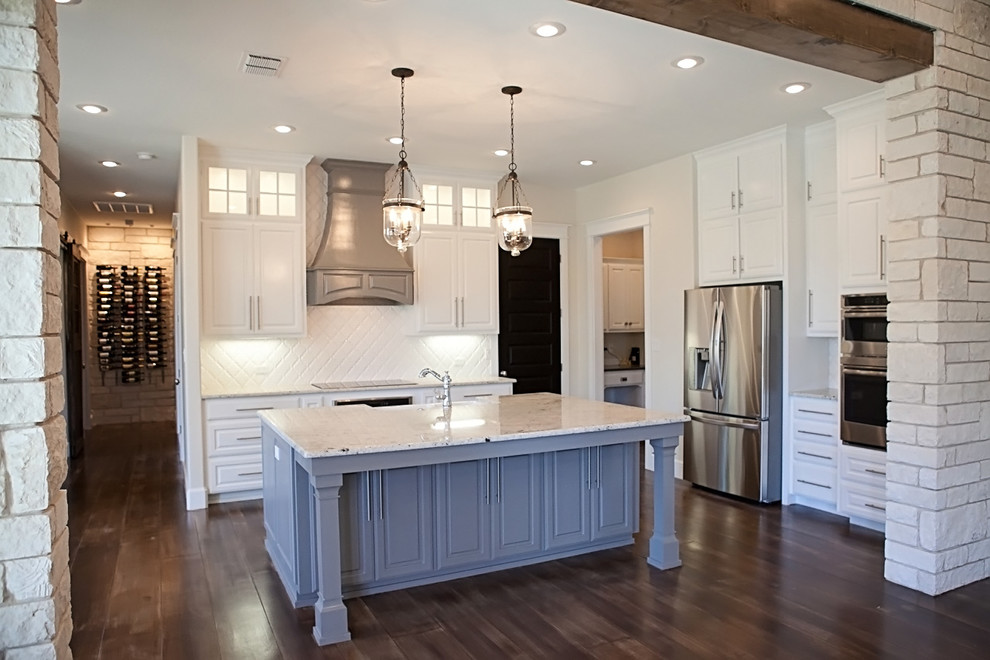 Design ideas for a large arts and crafts l-shaped eat-in kitchen in Austin with a farmhouse sink, raised-panel cabinets, white cabinets, granite benchtops, white splashback, ceramic splashback, stainless steel appliances, concrete floors and with island.