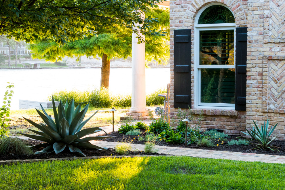 Immagine di un grande giardino classico esposto in pieno sole davanti casa in estate con pacciame e recinzione in metallo