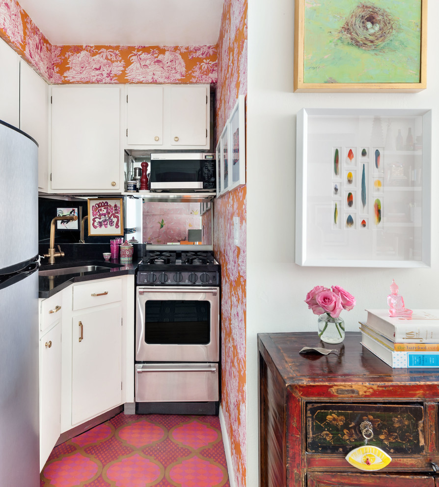 This is an example of a small eclectic open plan kitchen in New York with an undermount sink, flat-panel cabinets, white cabinets, black splashback, stainless steel appliances, no island, pink floor and black benchtop.