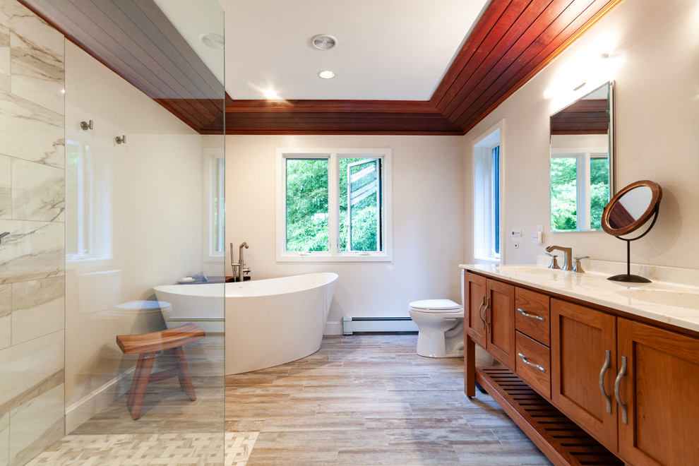 Photo of a large master bathroom in Boston with shaker cabinets, medium wood cabinets, a freestanding tub, a curbless shower, beige tile, marble, porcelain floors, an integrated sink, solid surface benchtops, brown floor, an open shower, white benchtops, a double vanity, a freestanding vanity and wood.