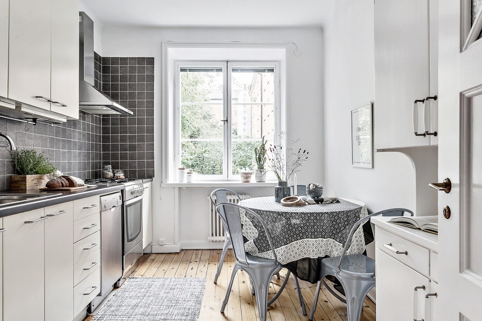 Exempel på ett avskilt skandinaviskt linjärt kök, med en nedsänkt diskho, släta luckor, vita skåp, grått stänkskydd, rostfria vitvaror, ljust trägolv och beiget golv