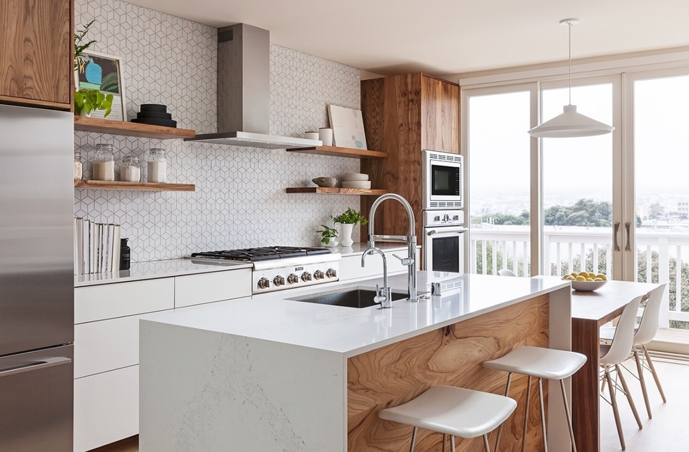 This is an example of a contemporary galley eat-in kitchen in San Francisco with an undermount sink, flat-panel cabinets, medium wood cabinets, white splashback, mosaic tile splashback, stainless steel appliances and with island.