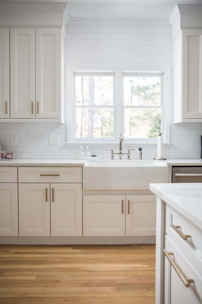 Design ideas for a mid-sized contemporary u-shaped eat-in kitchen in Atlanta with a farmhouse sink, recessed-panel cabinets, white cabinets, quartz benchtops, white splashback, ceramic splashback, stainless steel appliances, light hardwood floors, with island and white benchtop.