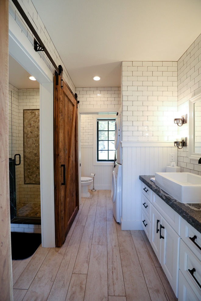 This is an example of a mid-sized transitional master bathroom in Other with recessed-panel cabinets, white cabinets, white tile, subway tile, soapstone benchtops, an open shower, a two-piece toilet, white walls, light hardwood floors, a vessel sink and a laundry.