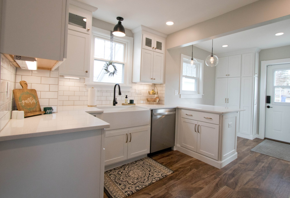 Inspiration for a mid-sized rustic galley vinyl floor and brown floor enclosed kitchen remodel with a farmhouse sink, recessed-panel cabinets, white cabinets, quartz countertops, white backsplash, subway tile backsplash, stainless steel appliances, a peninsula and white countertops