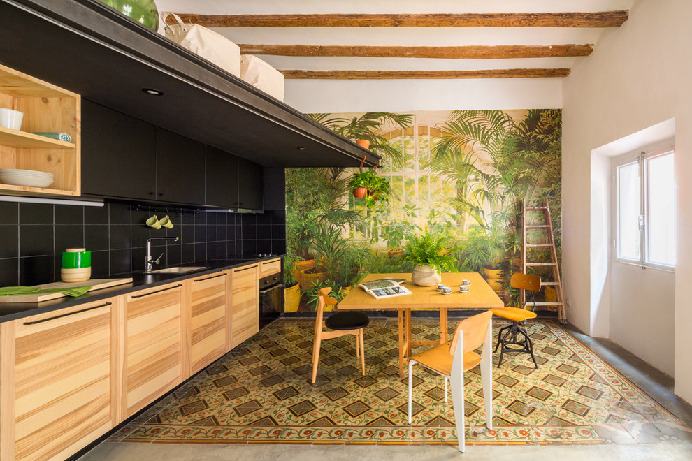Photo of a mid-sized tropical single-wall eat-in kitchen in Barcelona with an undermount sink, medium wood cabinets, black splashback, ceramic splashback, black appliances, ceramic floors, no island, multi-coloured floor and flat-panel cabinets.