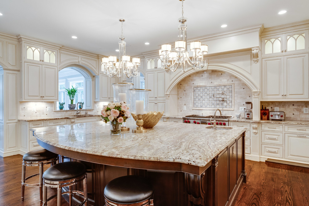 This is an example of a traditional u-shaped kitchen in DC Metro with raised-panel cabinets, white cabinets, granite benchtops, beige splashback, stone tile splashback, panelled appliances, dark hardwood floors, with island, brown floor, beige benchtop and an undermount sink.