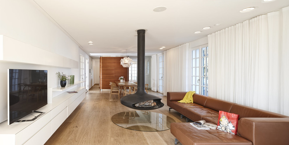 Design ideas for an expansive contemporary open concept living room in Stuttgart with light hardwood floors, a hanging fireplace and a metal fireplace surround.