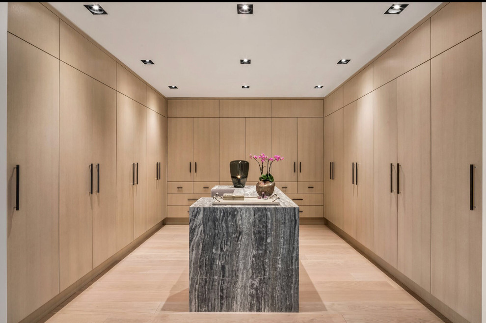 This is an example of a contemporary gender-neutral dressing room in New York with flat-panel cabinets, light wood cabinets, light hardwood floors and beige floor.
