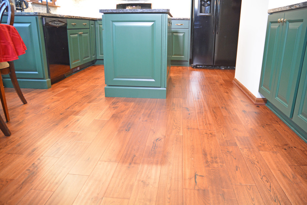Small transitional l-shaped medium tone wood floor and brown floor eat-in kitchen photo with an undermount sink, raised-panel cabinets, green cabinets, quartz countertops, white backsplash, marble backsplash, black appliances, an island and multicolored countertops
