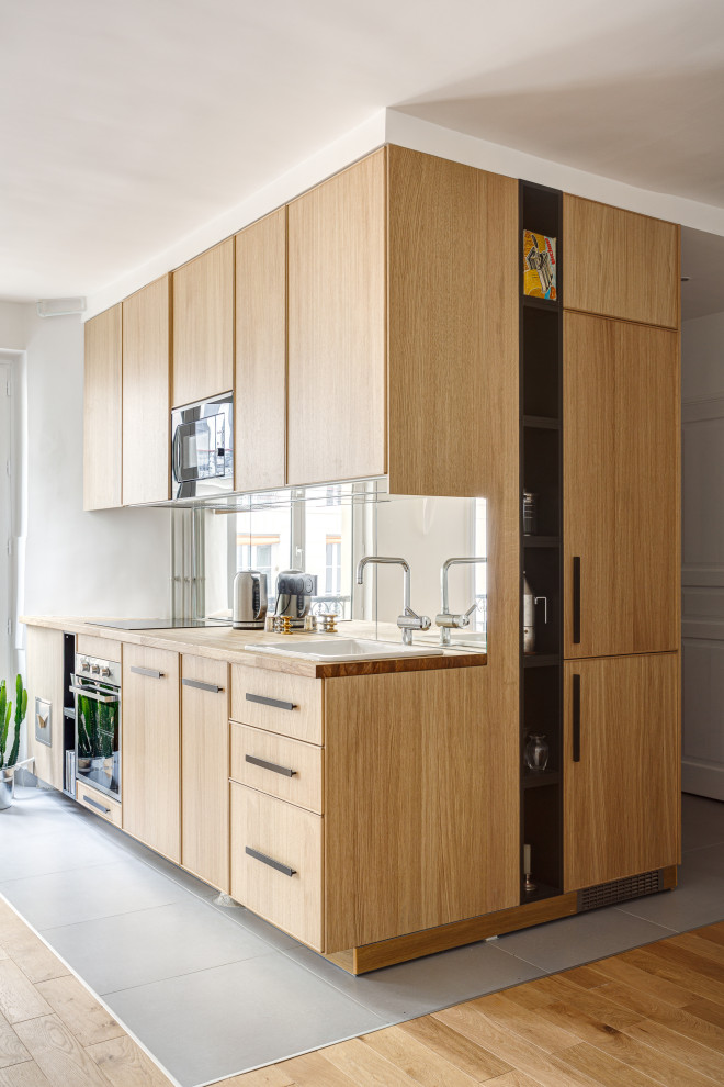 Design ideas for a small contemporary l-shaped kitchen in Paris with a drop-in sink, flat-panel cabinets, light wood cabinets, wood benchtops, mirror splashback, panelled appliances, porcelain floors, no island, grey floor and beige benchtop.