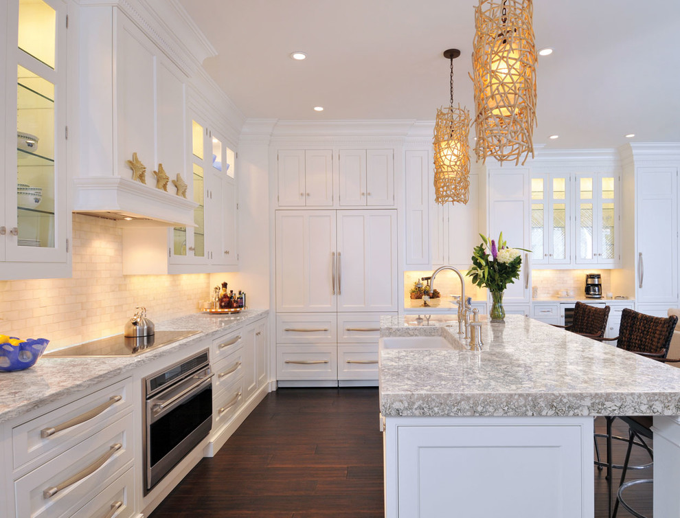 Photo of a beach style l-shaped kitchen in Other with a farmhouse sink, beaded inset cabinets, white cabinets, white splashback, panelled appliances, dark hardwood floors and with island.