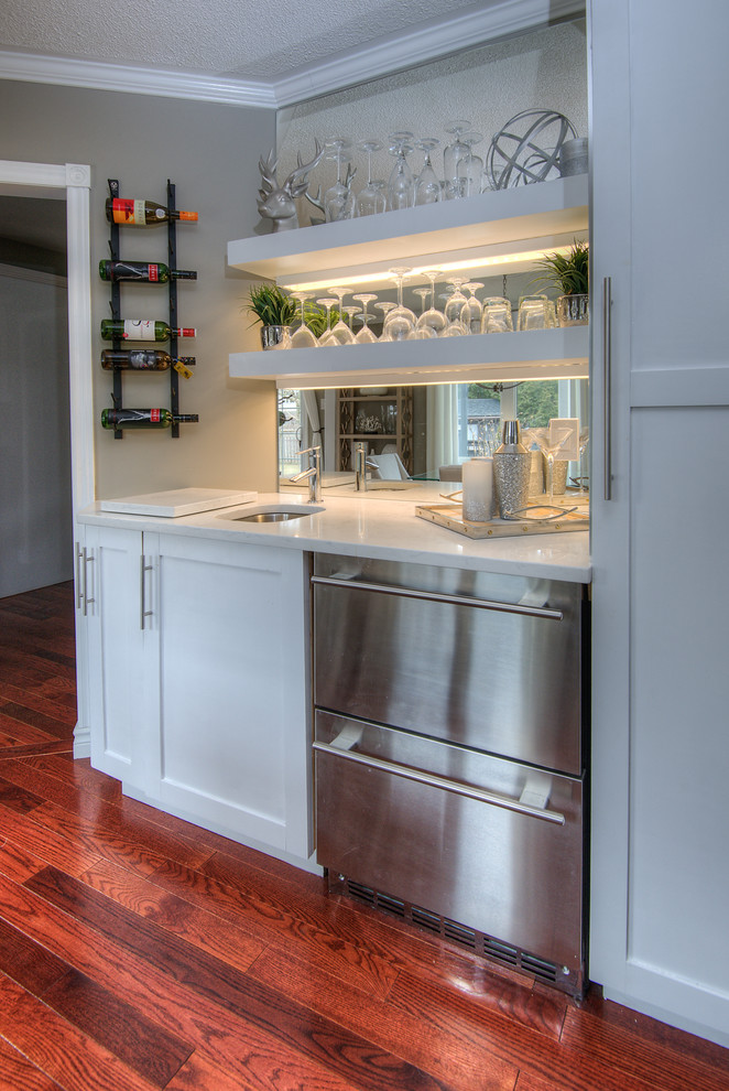 Photo of a small contemporary single-wall wet bar in Toronto with an undermount sink, shaker cabinets, white cabinets, quartz benchtops, mirror splashback, medium hardwood floors, brown floor and white benchtop.