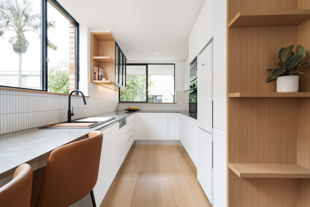 Geschlossene Moderne Küche ohne Insel in U-Form mit Waschbecken, weißen Schränken, Quarzwerkstein-Arbeitsplatte, Küchenrückwand in Weiß, Rückwand aus Keramikfliesen, braunem Holzboden und braunem Boden in Sydney