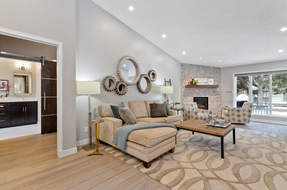 This is an example of a medium sized contemporary open plan living room in Calgary with a reading nook, grey walls, light hardwood flooring, a corner fireplace, a stone fireplace surround, beige floors and a freestanding tv.