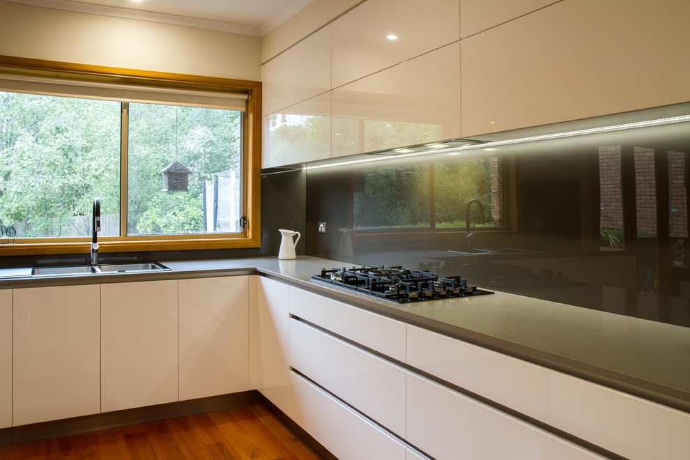 Photo of a large modern l-shaped eat-in kitchen in Melbourne with flat-panel cabinets, quartz benchtops, metallic splashback, glass sheet splashback, medium hardwood floors and with island.