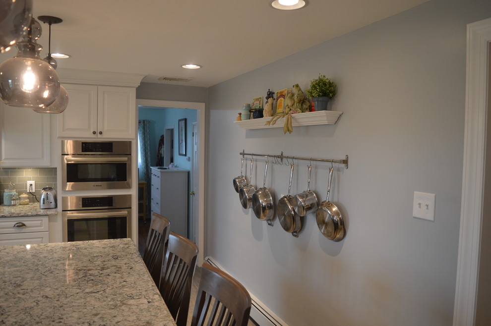 Example of a large transitional u-shaped ceramic tile and gray floor enclosed kitchen design with a farmhouse sink, raised-panel cabinets, white cabinets, quartz countertops, gray backsplash, glass tile backsplash, stainless steel appliances and an island