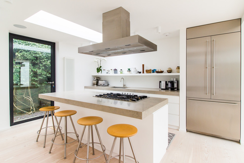 This is an example of a mid-sized contemporary kitchen in London with with island, an undermount sink, flat-panel cabinets, white cabinets, light hardwood floors, stainless steel appliances and beige floor.