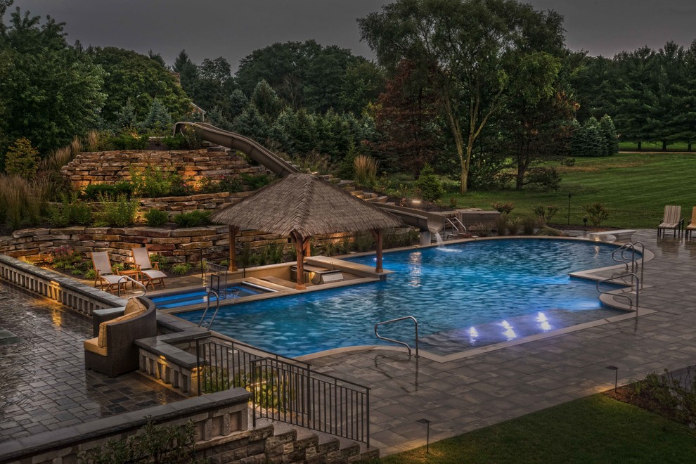 Photo of an expansive tropical backyard custom-shaped lap pool in Chicago with a water slide and natural stone pavers.