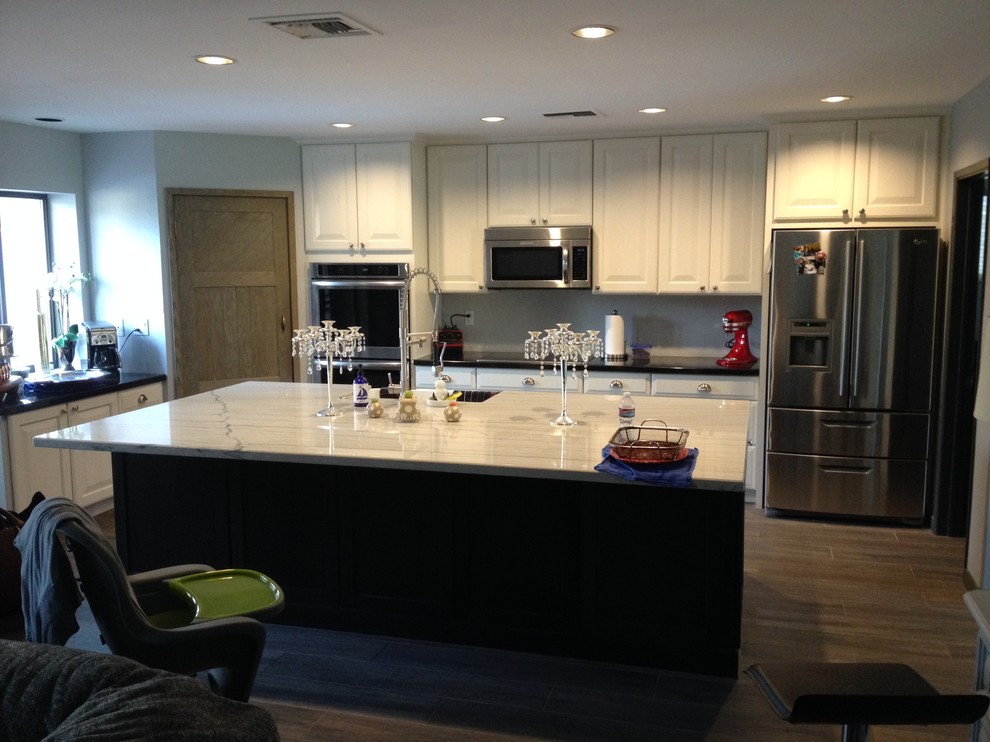 Mid-sized transitional u-shaped medium tone wood floor eat-in kitchen photo in Phoenix with a drop-in sink, raised-panel cabinets, white cabinets, granite countertops, white backsplash, ceramic backsplash, stainless steel appliances and an island