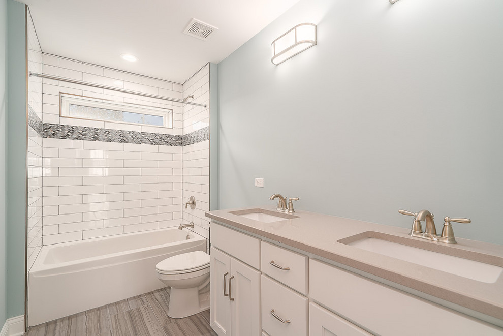 Design ideas for a mid-sized transitional bathroom in Chicago with recessed-panel cabinets, white cabinets, an alcove tub, a shower/bathtub combo, a two-piece toilet, white tile, subway tile, blue walls, porcelain floors, an undermount sink, engineered quartz benchtops, beige floor, a shower curtain and beige benchtops.