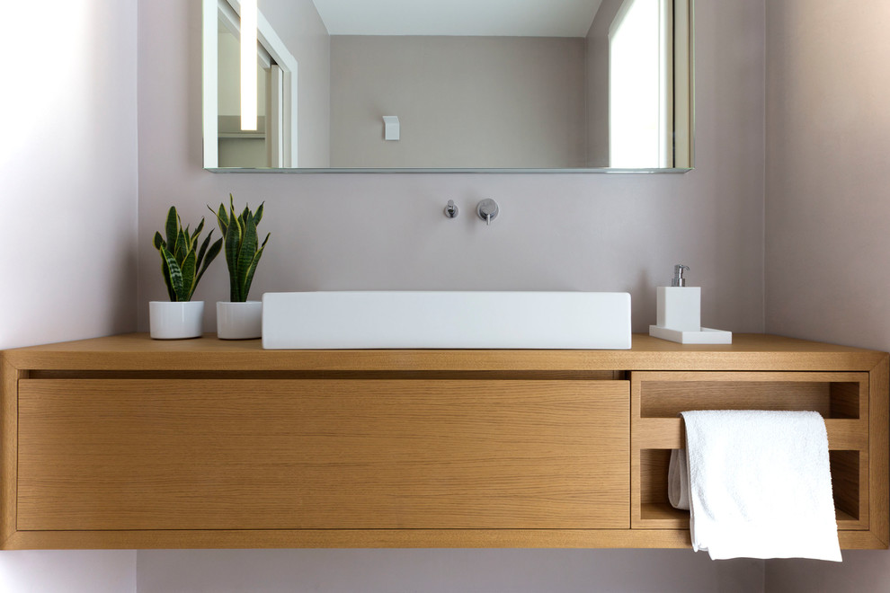 This is an example of a mid-sized contemporary powder room in Venice with light wood cabinets, a wall-mount toilet, beige walls, a vessel sink, wood benchtops, beige floor and brown benchtops.