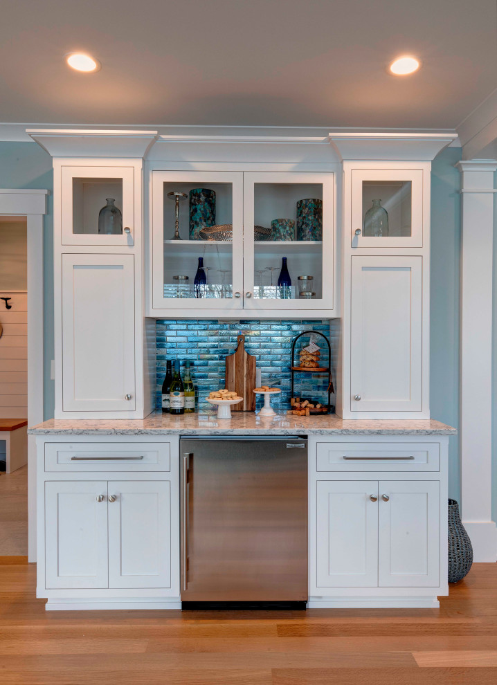 This is an example of a medium sized traditional single-wall dry bar in Boston with no sink, recessed-panel cabinets, white cabinets, quartz worktops, blue splashback, glass tiled splashback, light hardwood flooring, beige floors and grey worktops.