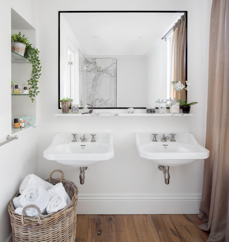 Design ideas for a transitional bathroom in London with a corner shower, gray tile, white walls, medium hardwood floors, a wall-mount sink, brown floor and a hinged shower door.