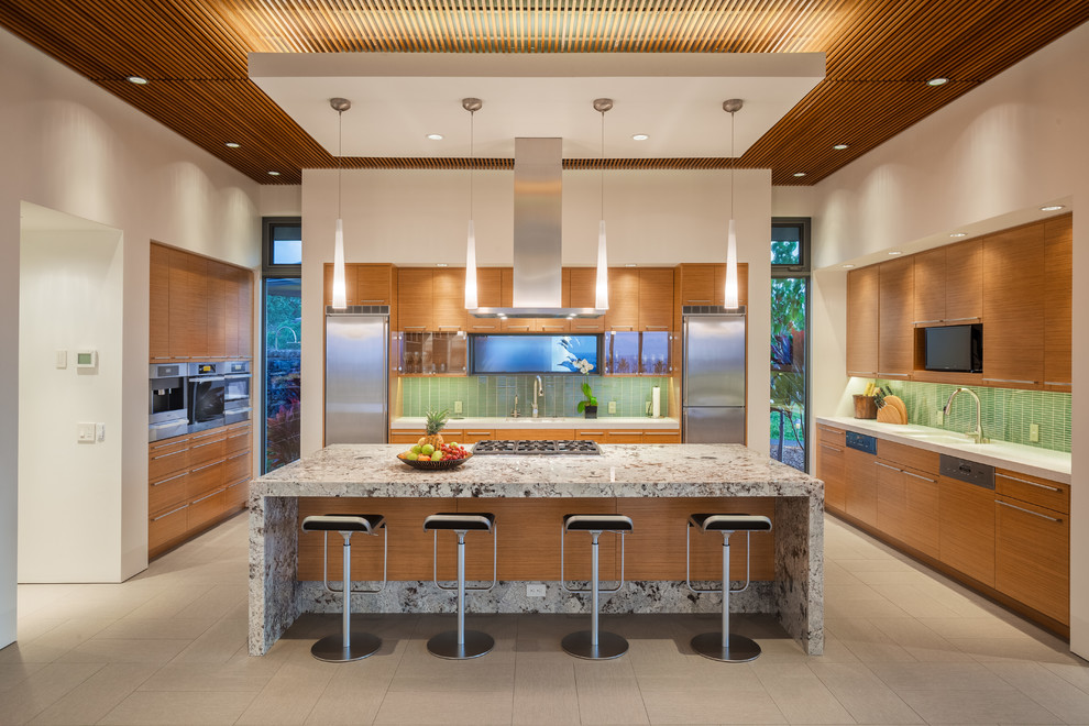 This is an example of a mid-sized tropical single-wall separate kitchen in Hawaii with flat-panel cabinets, medium wood cabinets, green splashback, glass tile splashback, with island, an undermount sink, granite benchtops, stainless steel appliances, porcelain floors and beige floor.