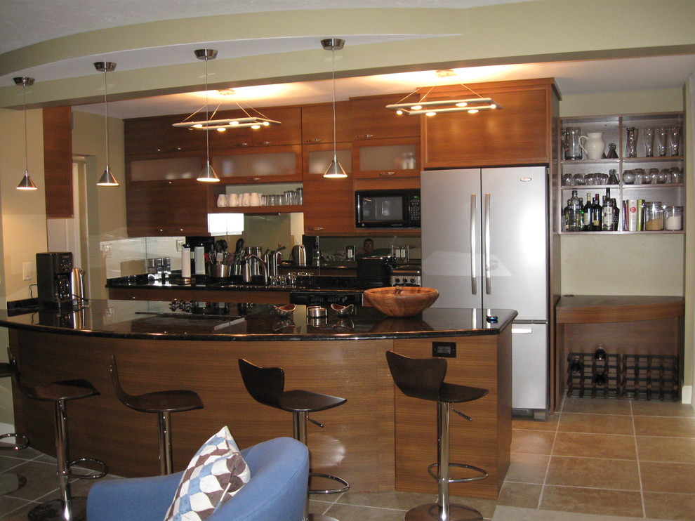 This is an example of a contemporary galley open plan kitchen in Miami with an undermount sink, flat-panel cabinets, medium wood cabinets, granite benchtops, mirror splashback, black appliances, ceramic floors and a peninsula.