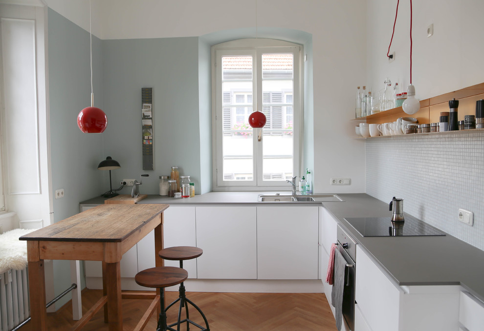 Schmale Küche ohne Insel in L-Form With Einbauwaschbecken, flächenbündigen Schrankfronten, weißen Schränken, Rückwand aus Mosaikfliesen, Küchengeräten aus Edelstahl, hellem Holzboden, Mineralwerkstoff-Arbeitsplatte and Küchenrückwand in Grau in Frankfurt